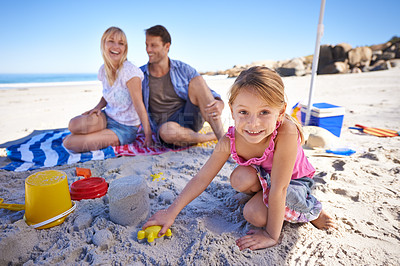 Buy stock photo Parents, girl and sandcastle in portrait by sea, blanket and excited with building for holiday in summer. Father, mother and daughter with family picnic by ocean for vacation with smile in sunshine