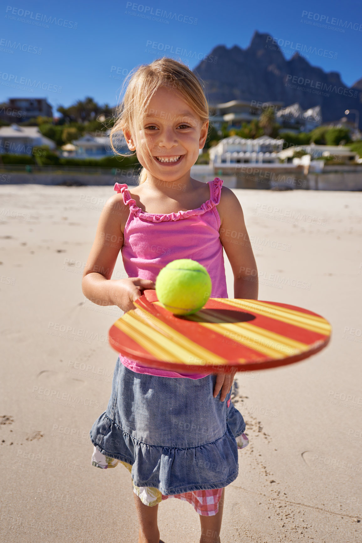 Buy stock photo Young girl, smile and tennis ball in beach with bat, playing and active outdoor. Child, motor skills and growth for development in ocean or sea with mountain view, sand and enjoying in summer