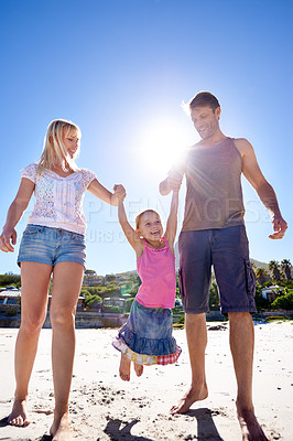 Buy stock photo Holding hands, love and happy family at a beach with swing, support and care while bonding in nature. Freedom, travel and kid with parents at the ocean for morning games, fun or adventure at the sea