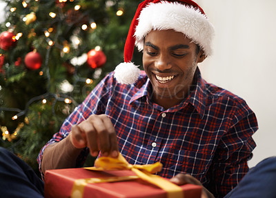 Buy stock photo Shot of a handsome young man unwrapping his Christmas present