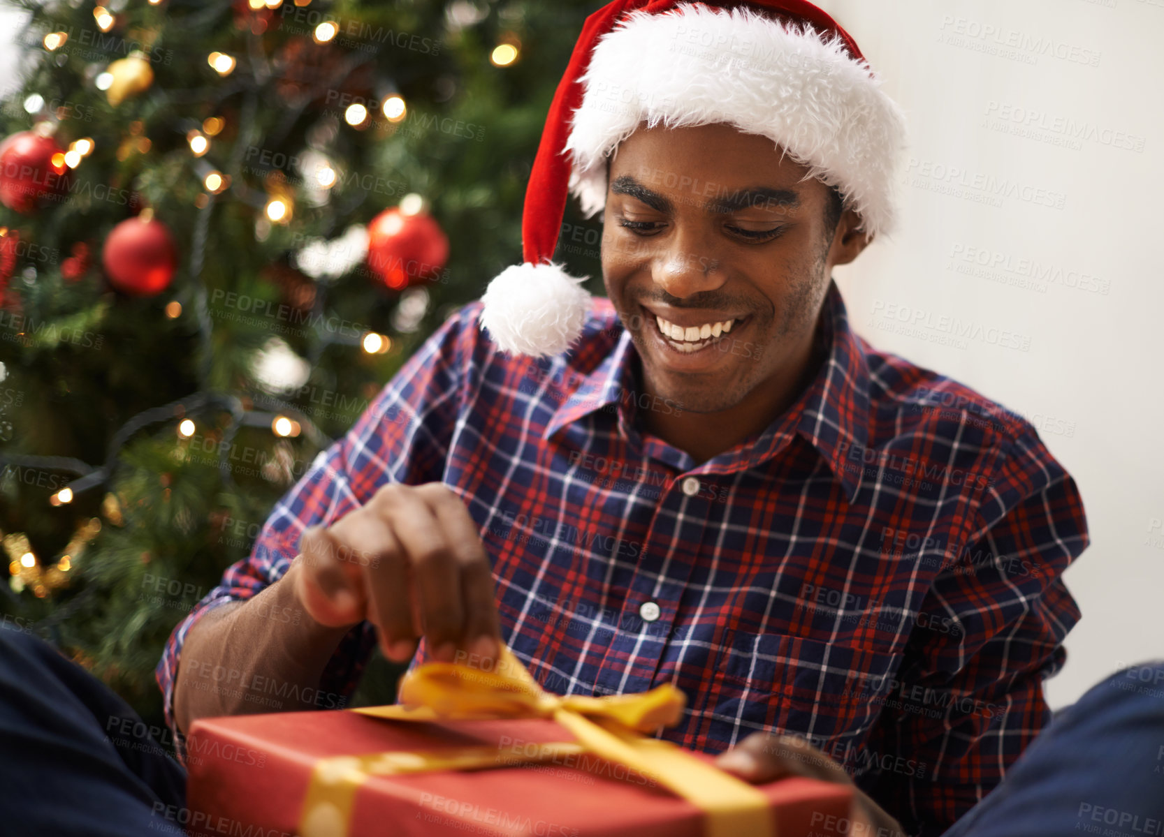 Buy stock photo Shot of a handsome young man unwrapping his Christmas present