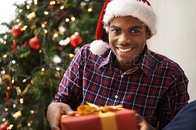 Buy stock photo African, man and gift for christmas, portrait and holiday with smile for vacation. Person, happiness and celebration for present, house and tree with decorations, giving or festivity at home with hat