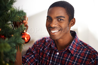 Buy stock photo Shot of a handsome young man standing by a christmas tree