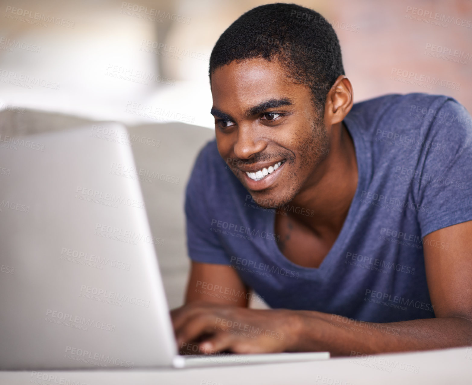 Buy stock photo Cropped shot of a handsome young man using his laptop while relaxing at home