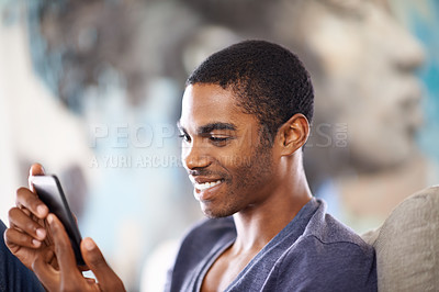 Buy stock photo Cropped shot of a handsome young man using his cellphone while chilling at home