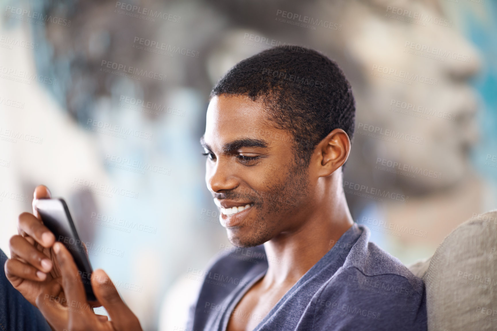 Buy stock photo Cropped shot of a handsome young man using his cellphone while chilling at home