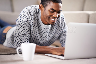 Buy stock photo Cropped shot of a handsome young man using his laptop while relaxing at home