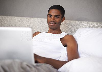 Buy stock photo Shot of a young man in bed using a laptop
