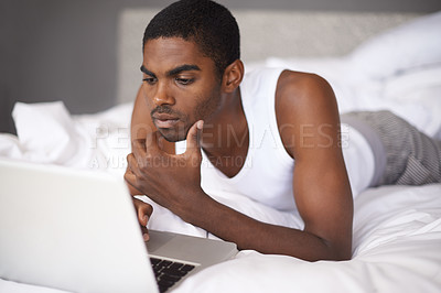 Buy stock photo Shot of a young man in bed using a laptop