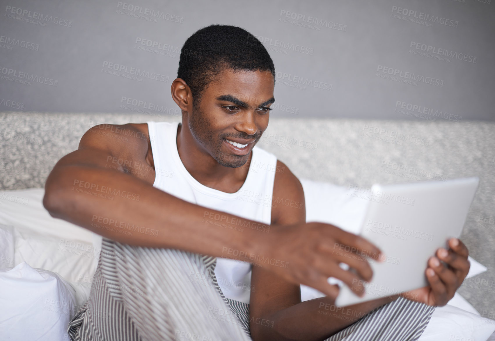 Buy stock photo Shot of a handsome young man using his tablet in bed