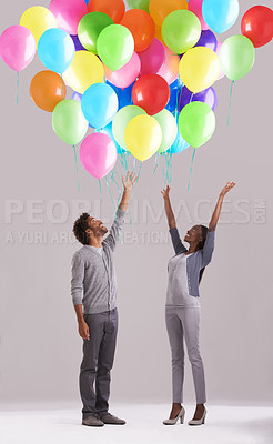 Buy stock photo Happy couple, party and celebration with balloons for event, birthday or romance on a gray studio background. Excited man and woman with colorful blowups of helium for date, giveaway or anniversary