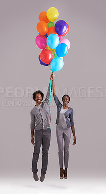 Buy stock photo Studio shot of a young couple holding a bunch of balloons as they float away