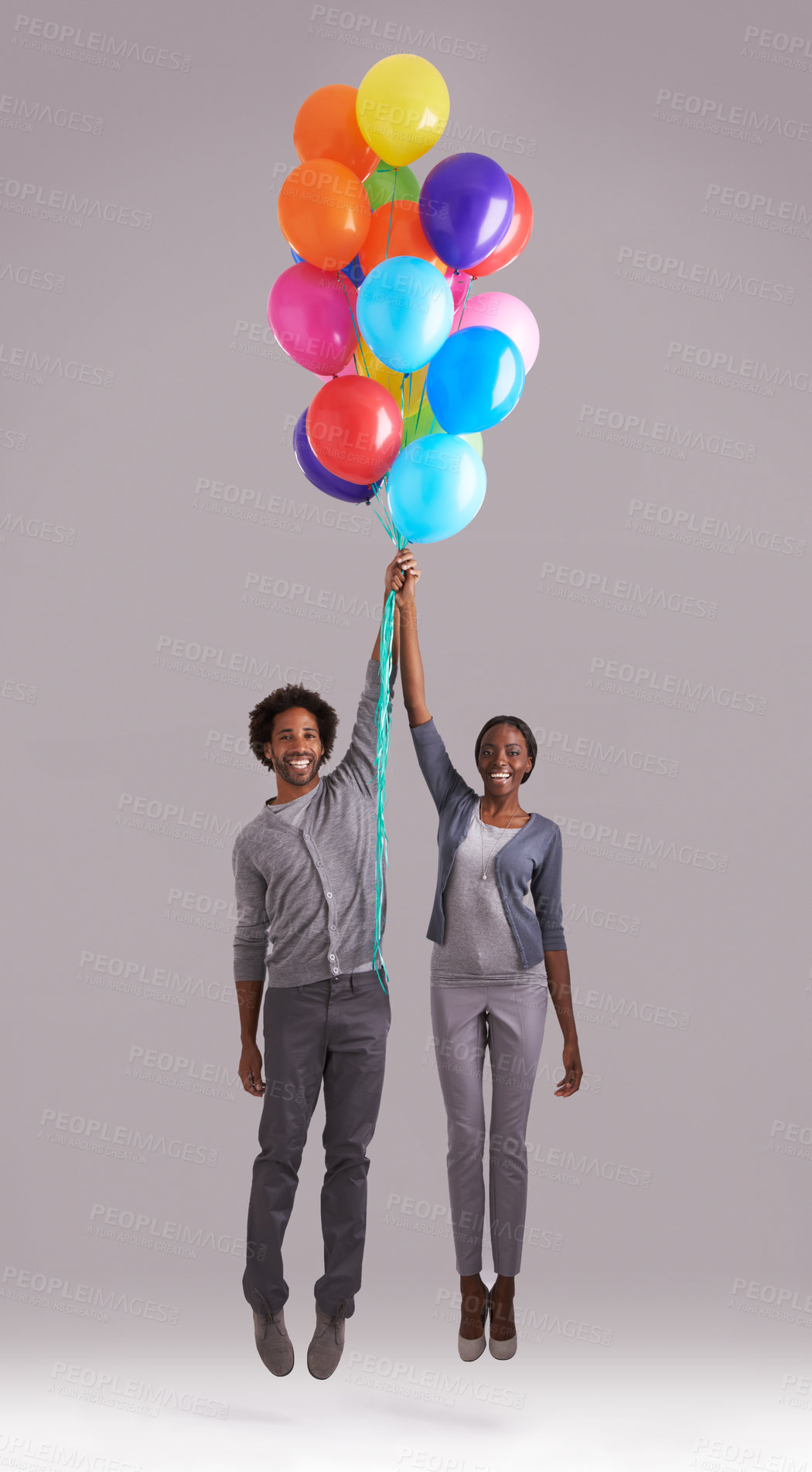 Buy stock photo Studio shot of a young couple holding a bunch of balloons as they float away