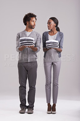 Buy stock photo Couple, laundry and teamwork in studio for helping, support and domestic chores on a white background. Serious African man and young woman with clothes in hands for fashion, neat and gender equality 