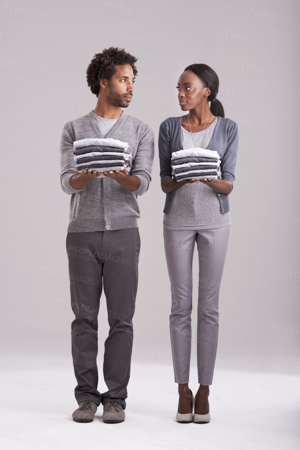 Buy stock photo Couple, laundry and teamwork in studio for helping, support and domestic chores on a white background. Serious African man and young woman with clothes in hands for fashion, neat and gender equality 