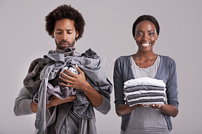 Buy stock photo Studio shot of a woman holding a neatly folded pile of clothes while her partner's is in a mess