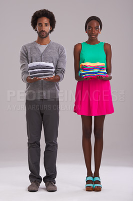 Buy stock photo Portrait, couple and folded clothes for laundry, fashion and cleaning in studio isolated on a gray background. African man, serious woman and fabric for housework, housekeeping or chores together