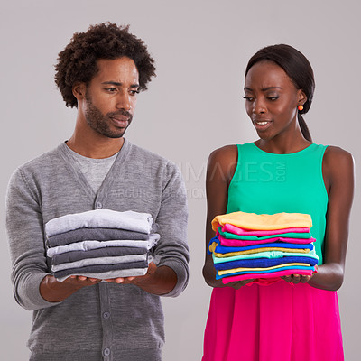 Buy stock photo People, studio and pile of laundry in hand for neat, wash day or cleaning clothes together. Couple, thinking and unsure of color choice for wardrobe with fashion, uncertain or ocd on grey background