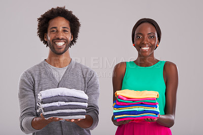 Buy stock photo Studio shot of a young man and woman each holding a neatly folded pile of clothes