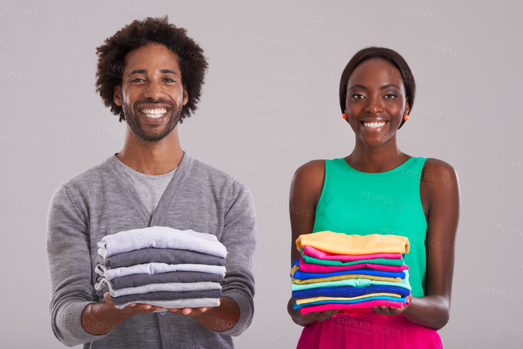 Buy stock photo Studio shot of a young man and woman each holding a neatly folded pile of clothes