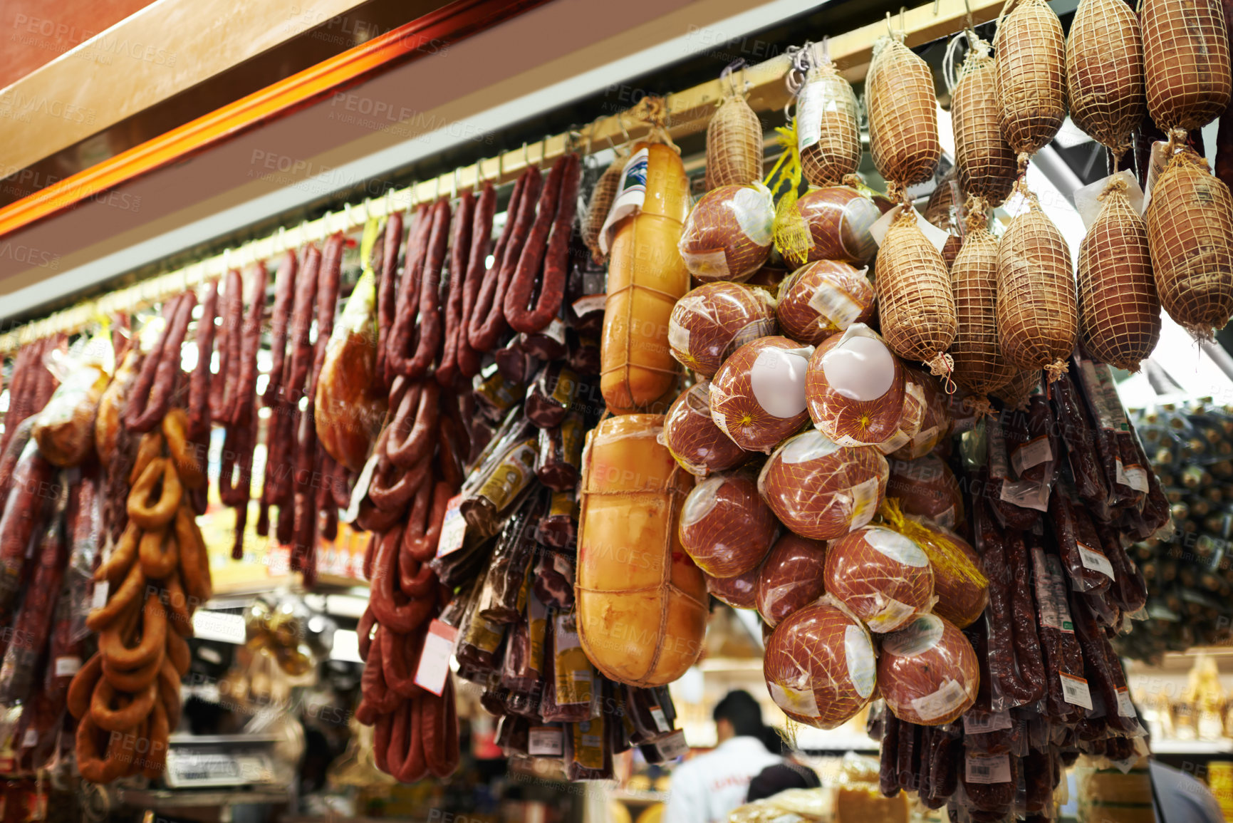 Buy stock photo Hooks, butcher and dry meat in shop for traditional food, groceries or products in Germany. Supermarket, deli and fermented or smoked sausages hanging in row for production in grocery store. 