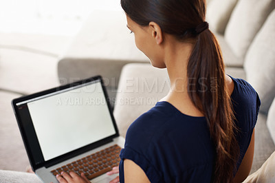 Buy stock photo Over the shoulder shot of a young woman using her laptop on her couch at home