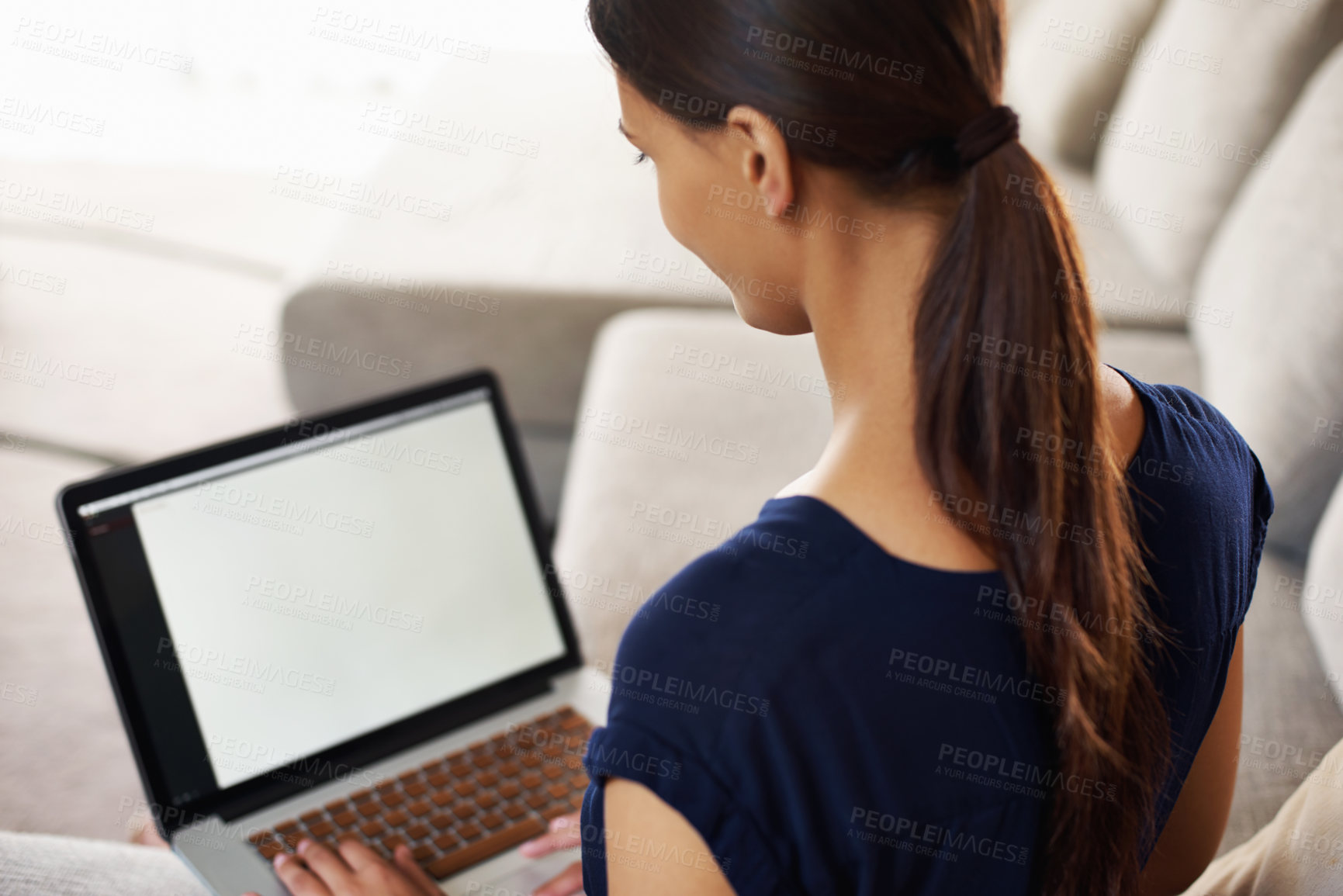 Buy stock photo Over the shoulder shot of a young woman using her laptop on her couch at home