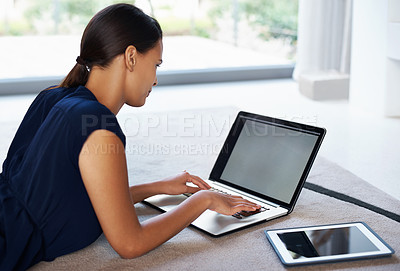 Buy stock photo Shot of an attractive young woman using her laptop and tablet while relaxing on the floor at home