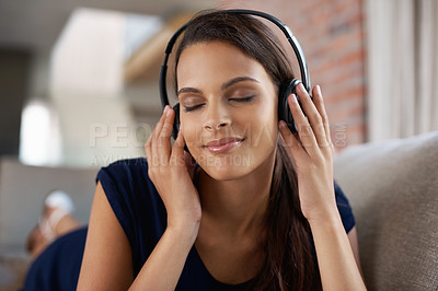 Buy stock photo Shot of a beautiful young woman lying on the sofa listening to music through headphones