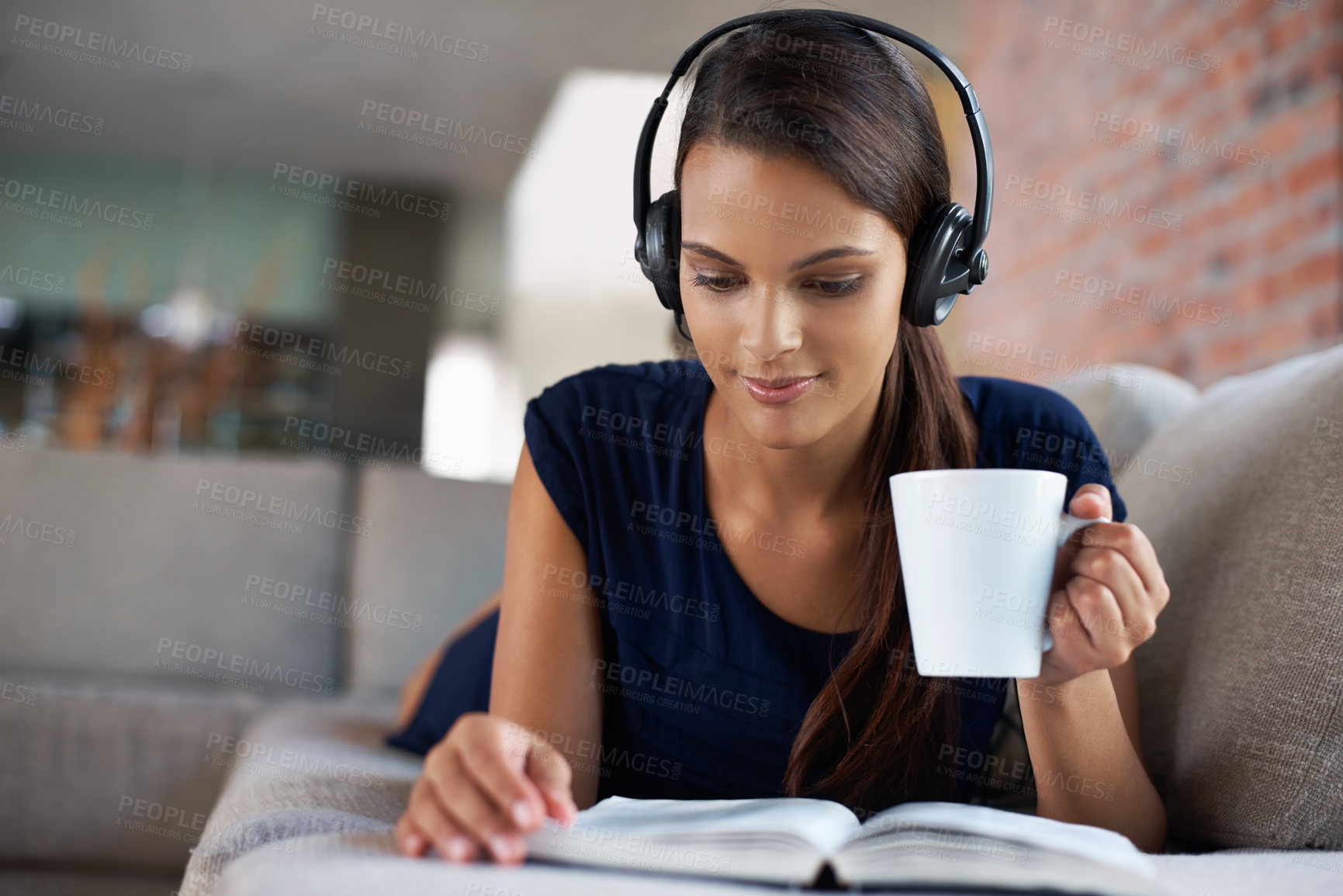 Buy stock photo Book, coffee and music with woman on sofa in living room of home, reading to relax at weekend. Storytelling, headphones and drinking tea with young person in apartment for hobby, leisure or time off