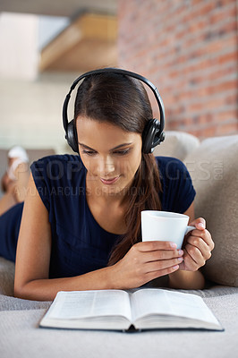 Buy stock photo Music, book and woman relax with coffee in home on holiday or vacation and headphones streaming audio. Girl, reading and listening to sound on sofa in apartment on weekend with green tea or drink