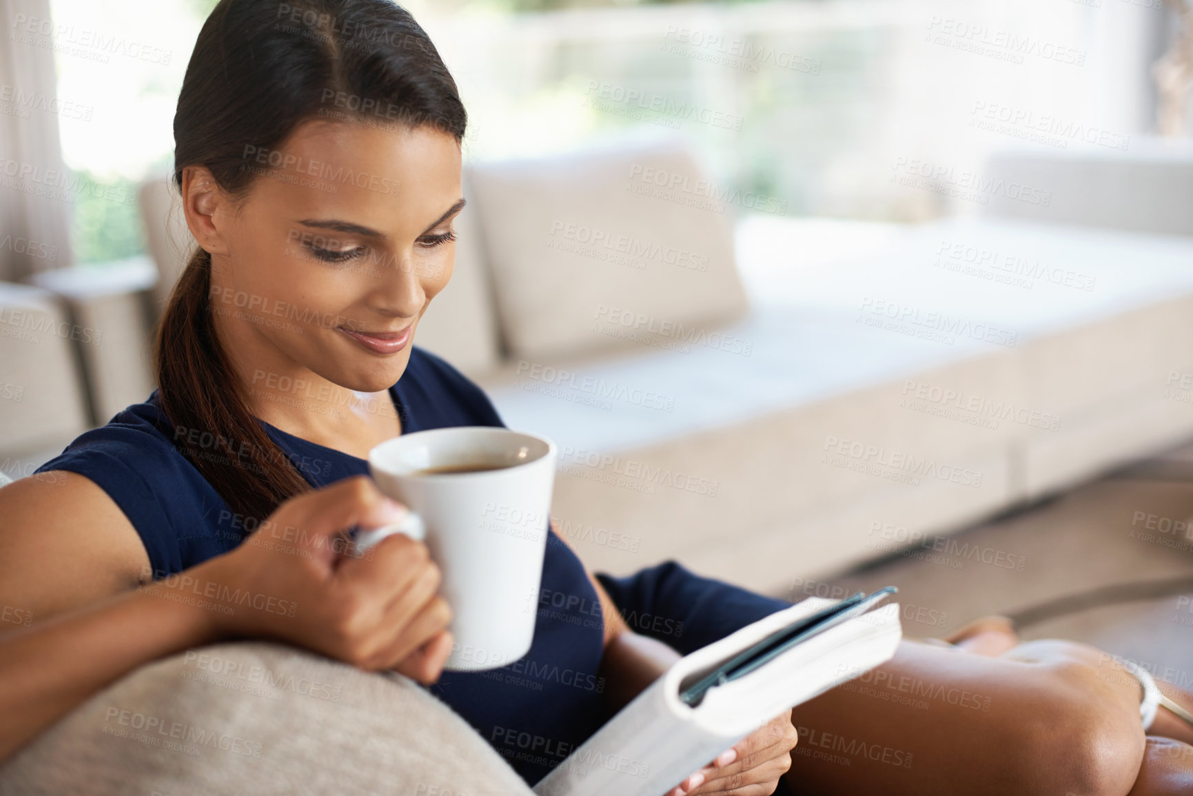 Buy stock photo Shot of a beautiful young woman relaxing with a book and a cup of coffee at home