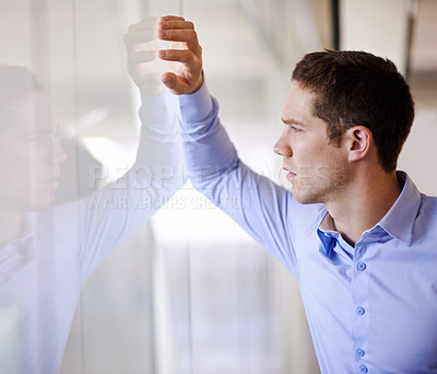 Buy stock photo A young businessman standing against a glass wall looking worried