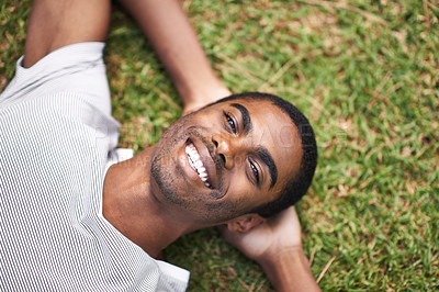Buy stock photo Portrait, smile and relax with black man on grass in garden to enjoy summer or nature outdoor. Face, field and green with happy young person in sunshine alone for peace, calm or quiet from above