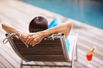 Buy stock photo Rear-view shot of a young woman relaxing on a deck chair by the poolside