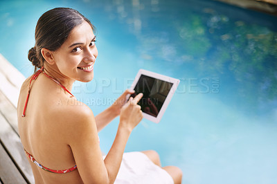 Buy stock photo Shot of a young woman relaxing by the pool with her tablet