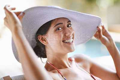 Buy stock photo Portrait of a smiling young woman sitting by a pool wearing a sunhat
