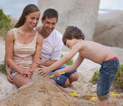 Buy stock photo Family, child and building sand castle at beach in summer for fun, travel or holiday with love. A man, woman and kid playing together on vacation at sea with a toy bucket, development and happiness