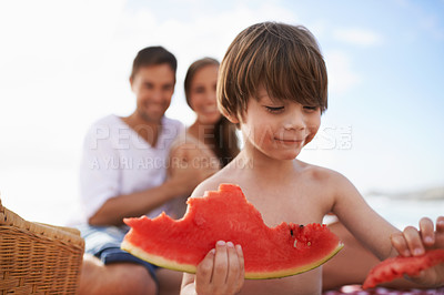 Buy stock photo A happy little boy biting into a watermelon with his parents looking on