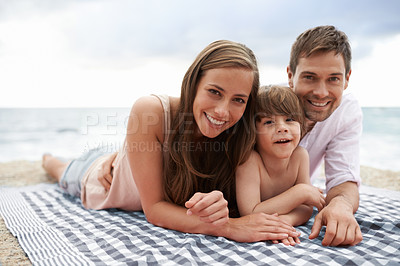 Buy stock photo Portrait of a happy young family lying on a beach blanket