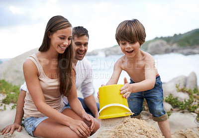 Buy stock photo Family, child and sand castle at beach in summer for fun, travel or holiday with a smile. A man, woman and excited kid playing together on vacation at sea with a toy bucket, development and happiness