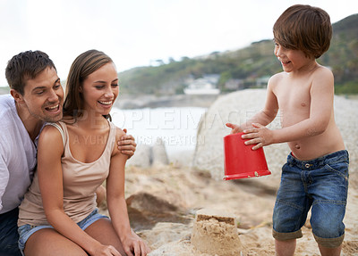Buy stock photo Child, family and sand castle at beach in summer for fun, travel or holiday with a smile. A man, woman and excited kid playing together on vacation at sea with a toy bucket, development and happiness