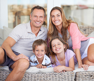 Buy stock photo Portrait of a happy young family of four sitting together on the patio