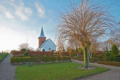 Buy stock photo Village church, graveyard or garden architecture for medieval christianity, landscape or historical building in Denmark. Chapel, place of worship or scenery and sky in nature for landmark or religion