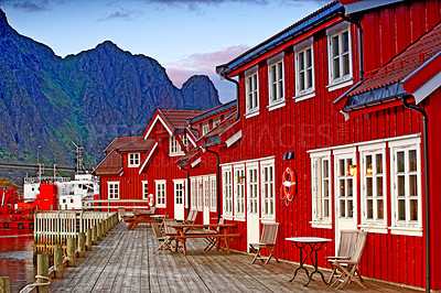 Buy stock photo Harbour town houses in Scandinavia. Small fishing village by a lake with bright red buildings. Peaceful background scene of maritime town with blue mountain and sky in Svolvaer, Lofoten, Norway