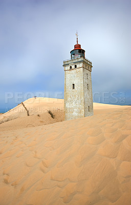 Buy stock photo Lighthouse on a sand dune by the sea against a blue sky. Mysterious old tower alone in the desert. Deserted lighthouse isolated on beige sand. Peaceful and tranquil nature scene in Jutland, Denmark.