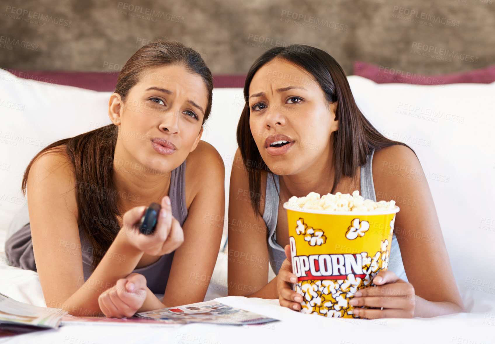 Buy stock photo Television, remote control and confused women on a bed with popcorn, movie or film in their home together. Watching tv, face and friends in a bedroom with theatre snack for Netflix, video or show