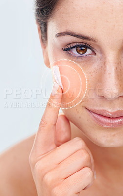 Buy stock photo Studio portrait of a a beautiful young woman applying moisturizer to her cheek