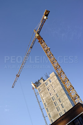 Buy stock photo Crane, construction and site on blue sky background for building with heavy machinery in architecture or engineering. Hoist in city, urban or industrial development in low angle of overhead equipment