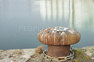 Buy stock photo A bollard port by a harbour. Rusty mooring bollard cast iron at pier shore. Sky and water background copyspace. Securing anchor point to prevent vessels from drifting away due tide, current and wind